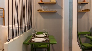 Un pasillo estrecho con una mesa de comedor preparada para dos, un banco verde y un espejo en la pared derecha.