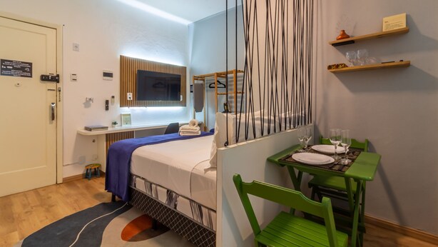 Habitación de hotel con cama, escritorio con computadora, silla, mesa para dos personas y ventana.