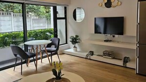 Ett modernt vardagsrum med ett runt bord, stolar, en tv och ett stort fönster.