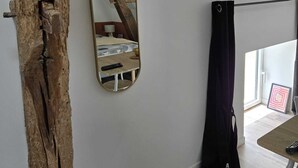 Ein Zimmer mit einem Holzbalken, einem Spiegel, einem Bett, einem Fenster mit Vorhang und einer Tür.