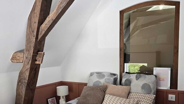 Ein Schlafzimmer mit schrägen Wänden, einem Bett mit gemusterten Betttextilien, einem Spiegel und einer Wandleuchte.