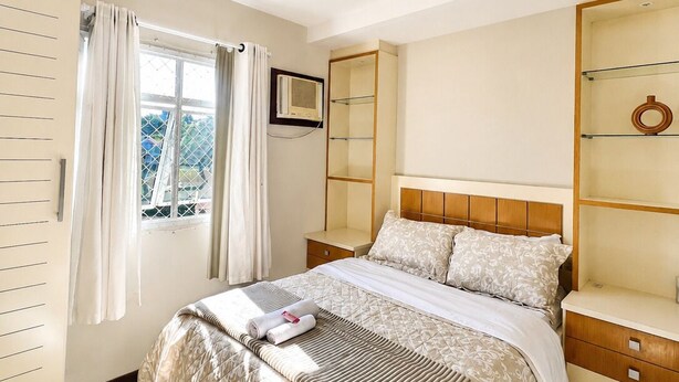 Une chambre à coucher comprenant un lit, une table de chevet, une armoire, une fenêtre avec des rideaux et un luminaire au plafond.