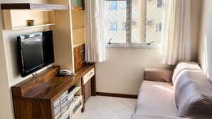 Un salon moderne avec un téléviseur, un meuble de rangement en bois, un canapé et une fenêtre avec des rideaux.
