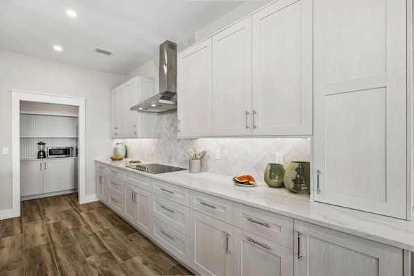 A kitchen with white cabinets, a stainless steel range hood, a microwave, and a sink.