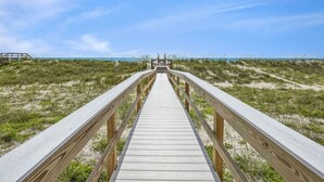 Een houten looppad naar een strand met duinen en een heldere lucht.