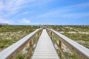 A wooden boardwalk leading to a beach with dunes and a clear sky.