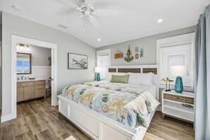 A bedroom with a bed, a vanity, a ceiling fan, and a window with blinds. - Driftwood Dunes | Brand New Oceanfront Beach House | Hot Tub | Elevator | EV Charger | Sleeps 17 (Fernandina Beach)