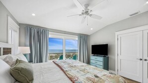Een slaapkamer met een bed, een televisie, een kledingkast en een balkon met uitzicht op zee.