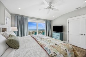 A bedroom with a bed, a television, a wardrobe, and a balcony with a view of the sea.