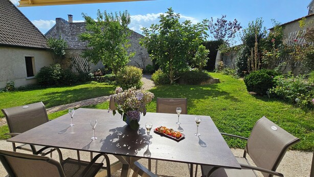 Eine Außenpatio mit einem Esstisch, umgeben von Stühlen, und ein Garten mit einem Steinhaus im Hintergrund.