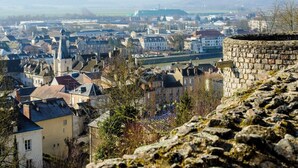 Eine Stadt mit historischen Steinmauern, einem Fluss und einer Mischung aus Wohn- und Geschäftsgebäuden.