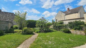 Ein Steinhaus mit einem gepflasterten Weg, der zu einer grünen Fläche mit Bäumen und blauem Himmel führt.