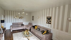Ein Wohnzimmer mit gestreifter Tapete, einer Kristallleuchtre, einem Sofa und einem Couchtisch.