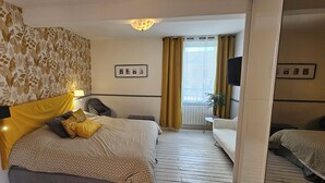 Ein Hotelzimmer mit Bett, Schreibtisch, Stuhl, Fernseher und einem Balkon mit Vorhängen.