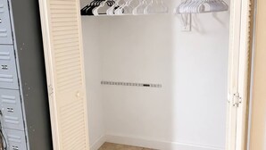 Un armario amplio con una barra de madera, múltiples perchas blancas y un archivador de metal.