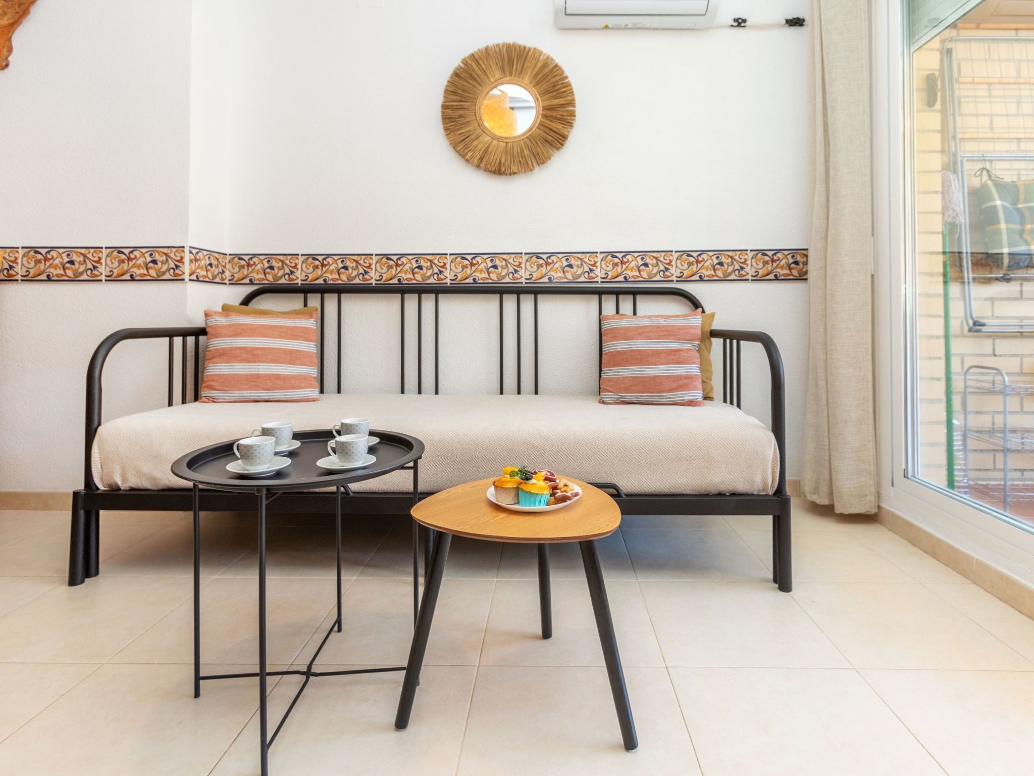 A sofa with a patterned border, a small round table with a tray, and a wall-mounted mirror.