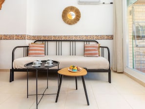 Ein Sofa mit gemustertem Rand, ein kleiner runder Tisch mit Tablett und ein an der Wand befestigter Spiegel.