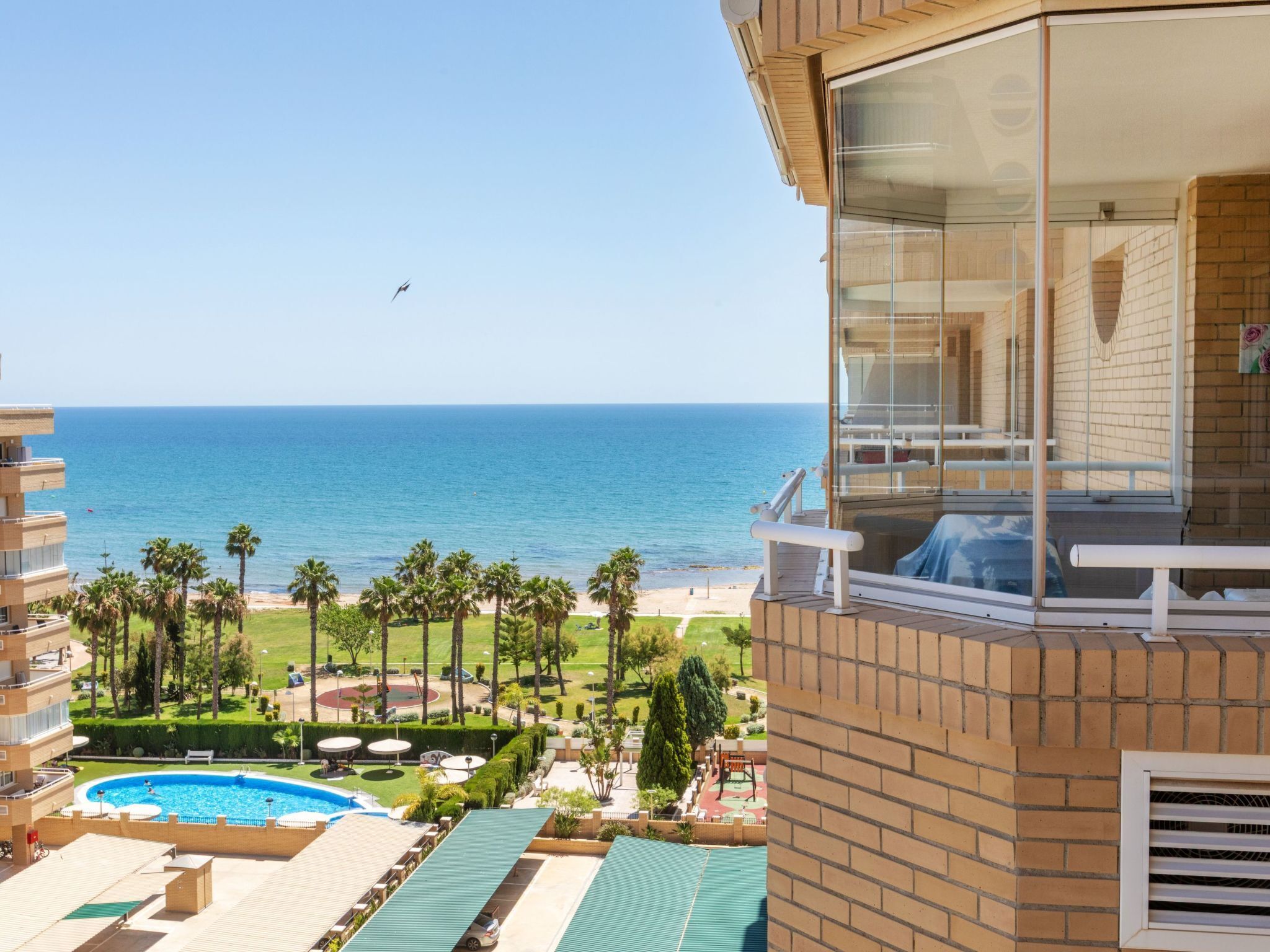 Un balcon d’hôtel avec vue sur l’océan, une piscine et un espace de jeux pour enfants.