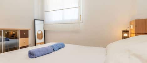 Habitación de hotel con cama, escritorio, espejo, ventana con cortinas y lámpara de noche.
