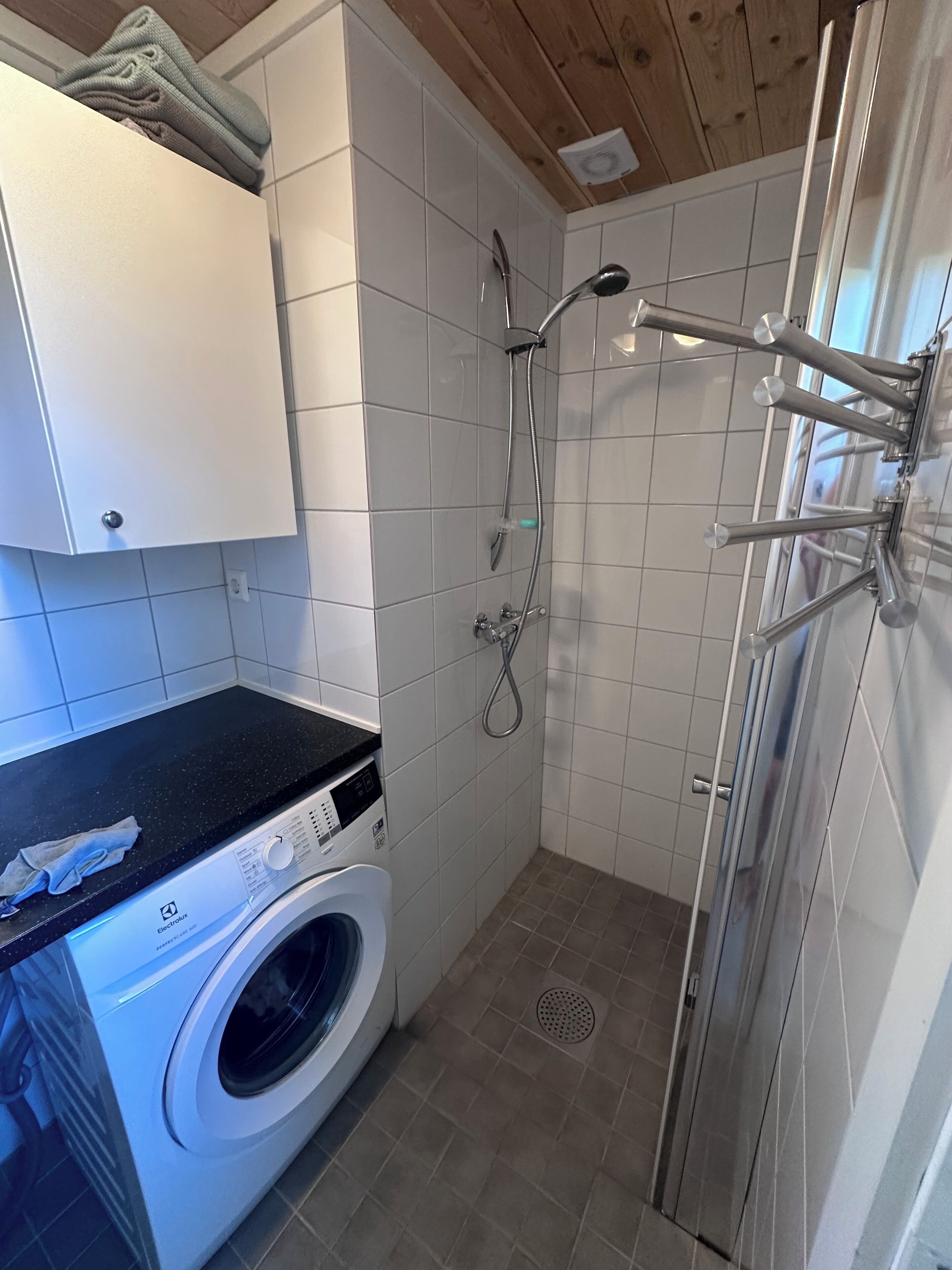 Un baño pequeño con lavadora, ducha con varios rociadores y paredes de azulejos.