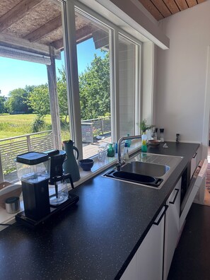 A kitchen with a large window, a coffee maker, a sink, and a view of a green landscape. - A large cabin on the outskirts of Tromøya, with Raet National Park as its closest neighbor. (Agder)