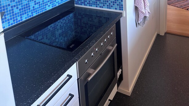 A kitchen with a black countertop, white cabinets, a blue tiled backsplash, and a hanging rack with towels. - A large cabin on the outskirts of Tromøya, with Raet National Park as its closest neighbor. (Agder)