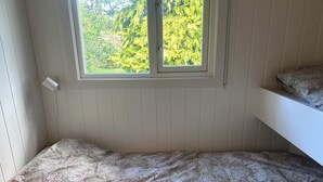 A single bed with a floral bedspread, a window with a view of greenery, and a wooden headboard. - A large cabin on the outskirts of Tromøya, with Raet National Park as its closest neighbor. (Agder)