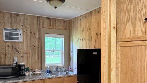 Une cuisine avec des meubles en bois, un réfrigérateur noir, un four à micro-ondes et une fenêtre donnant sur un paysage verdoyant.