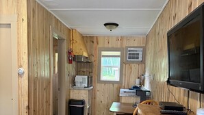 A compact room with a kitchenette, a television, and a bed with a checkered blanket.