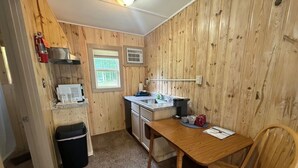A compact kitchen with wooden walls, a sink, a stove, and a dining area with a table and chairs.