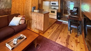 Interior de una cabaña con techo de madera, una cocina, una mesa de comedor y un sofá.
