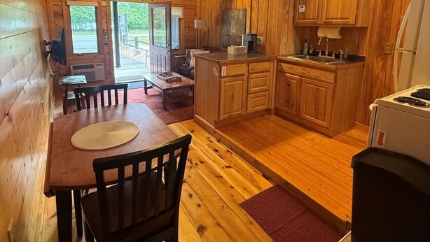 Interior de una cabaña de madera con comedor, cocina y vistas al exterior.