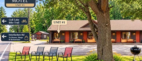 A motel named Gull Lake Motel with a sign indicating Unit #1. There are outdoor chairs and a barbecue grill in front.