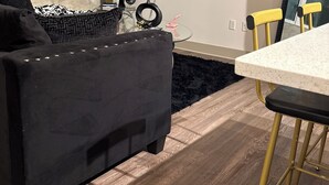 Ein modernes Wohnzimmer mit einem schwarzen Sofa, einem Glastisch, einem an der Wand befestigten Fernseher, einem gerahmten Bild und einem gelben Sessel.