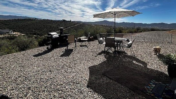 An outdoor seating area with tables and chairs, a large umbrella, and a gravel ground.