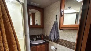 A compact RV bathroom with a window, a sink, a toilet, and a mirror.