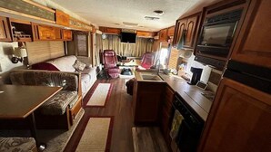A compact RV interior with a kitchenette, a dining area, and a seating area.