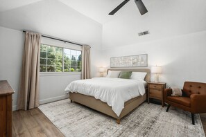 A bedroom with a bed, nightstands, a chair, a window with curtains, and a ceiling fan. - Yosemite 25 Min · Hot Tub · Game Room · Sleeps 8 (Oakhurst)