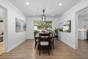 Un espace repas comprenant une longue table, des chaises, un lustre et un tableau accroché au mur.