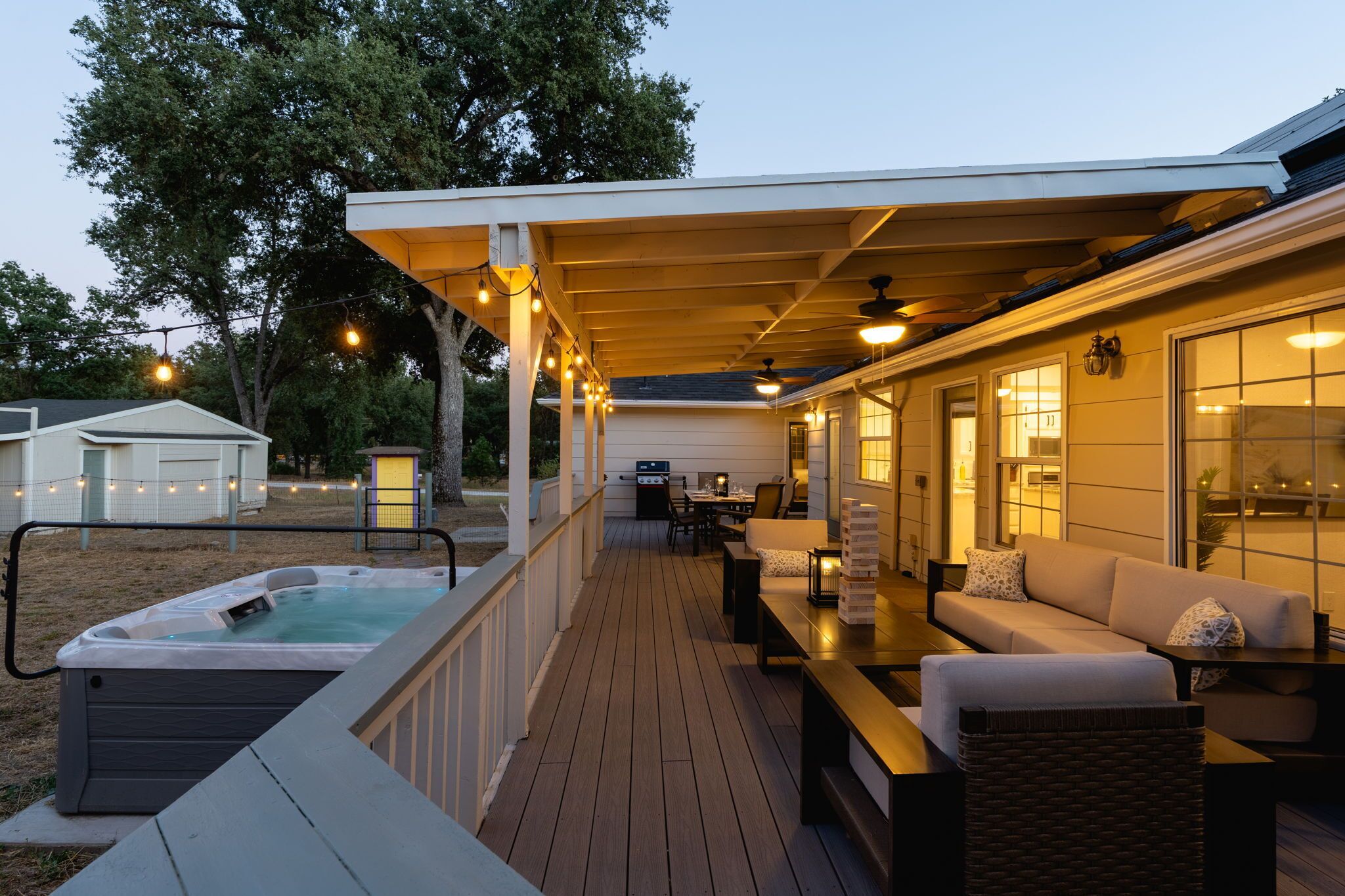 A covered outdoor deck with a hot tub, seating area, and a barbecue grill.