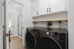 A laundry room with two front-loading washing machines, white cabinets above, and a wooden floor. - Yosemite 25 Min · Hot Tub · Game Room · Sleeps 8 (Oakhurst)