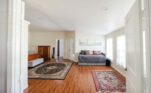 Un salon spacieux doté d’un parquet, d’un canapé gris, d’une armoire en bois et d’un grand tapis.