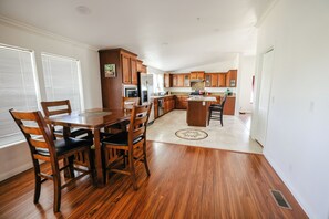 A spacious kitchen with wooden cabinets, a central island, and a dining area with chairs. - Spacious Orchard Retreat with Golf Course Views & Large Patio (Moorpark)