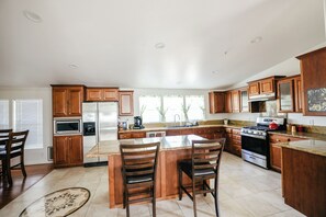 A kitchen with wooden cabinets, a refrigerator, a stove, and a dining area with chairs. - Spacious Orchard Retreat with Golf Course Views & Large Patio (Moorpark)