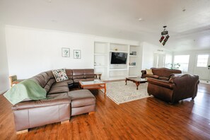 A living room with a brown leather sectional sofa, a brown armchair, a glass coffee table, and a patterned rug. - Spacious Orchard Retreat with Golf Course Views & Large Patio (Moorpark)