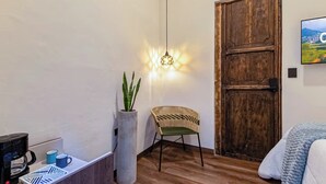 A room with a wooden door, a potted plant, a wicker chair, a bed, a coffee maker, and a wall-mounted TV. - Casa Boutique WeLoft  San Antonio Cali (Cali)