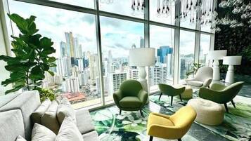Una sala de estar moderna con vistas a la ciudad, sillones verdes y amarillos, y una planta grande.