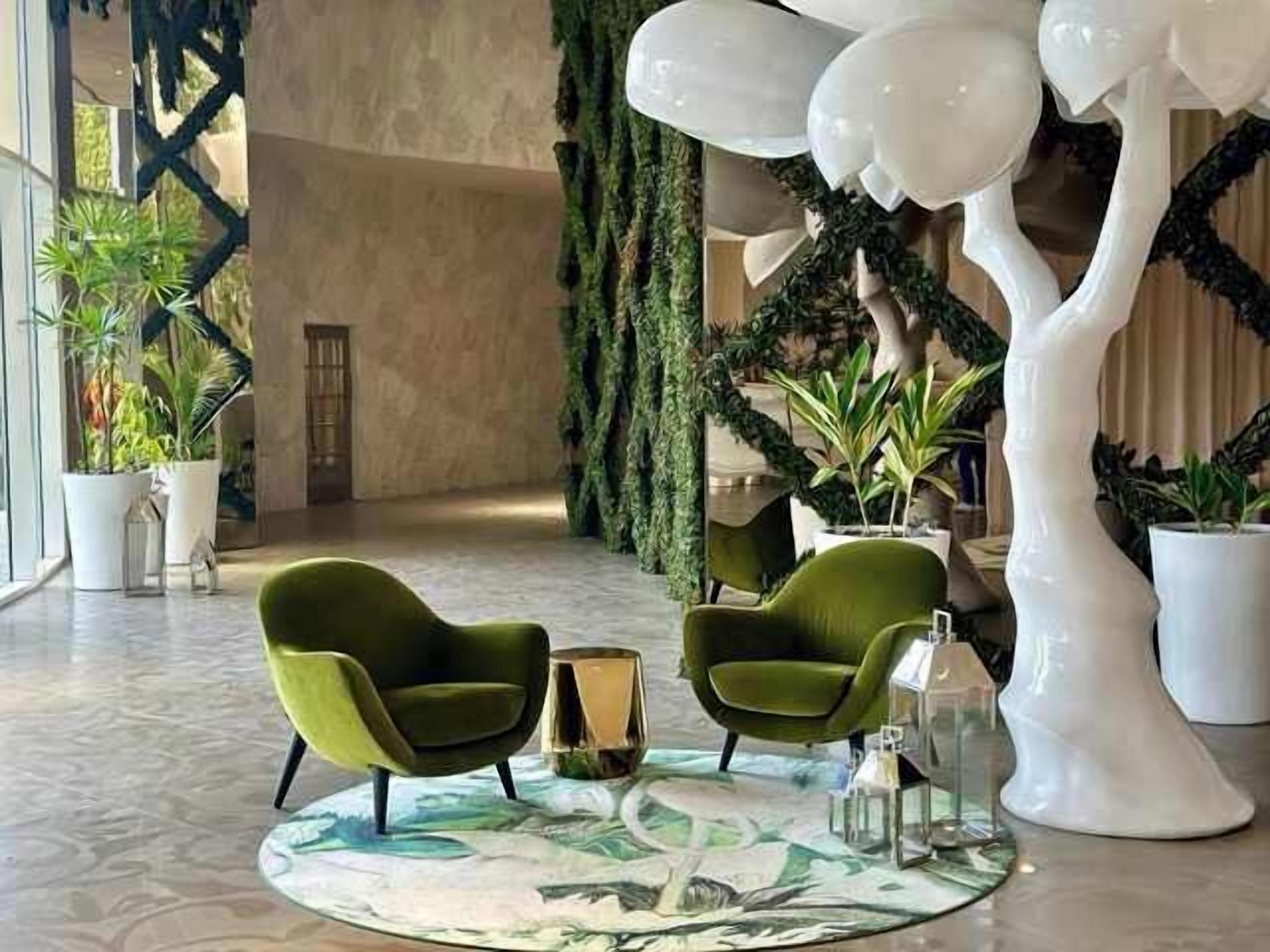 Un hall con dos sillones verdes, una mesa redonda y una gran escultura de árbol blanco.