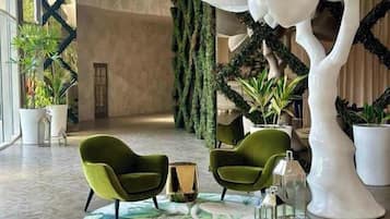 Un hall con dos sillones verdes, una mesa redonda y una gran escultura de árbol blanco.