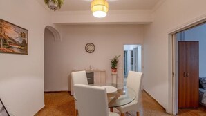 Een eethoek met een glazen tafel, witte stoelen, een klok en een deur naar een andere kamer.